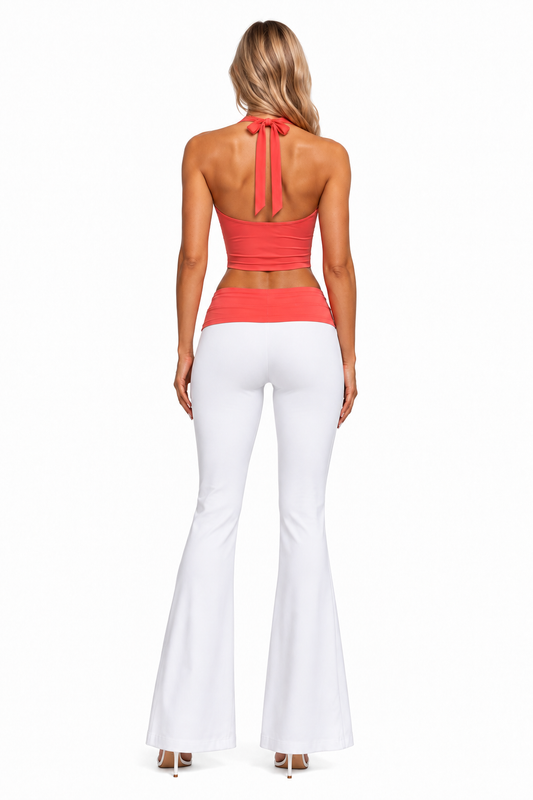 A woman shown from the back wearing a coral halter crop top with a tie-back and white flared pants, photographed against a plain white studio background.